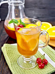 Lemonade with cherries in wineglass and jug on dark board