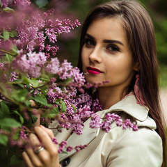 beautiful young woman in a trench coat near blooming lilac