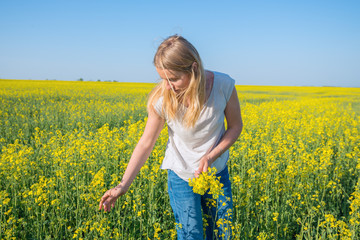 Fototapeta premium Cute girl, blonde collects yellow flowers in a field under a blue sky