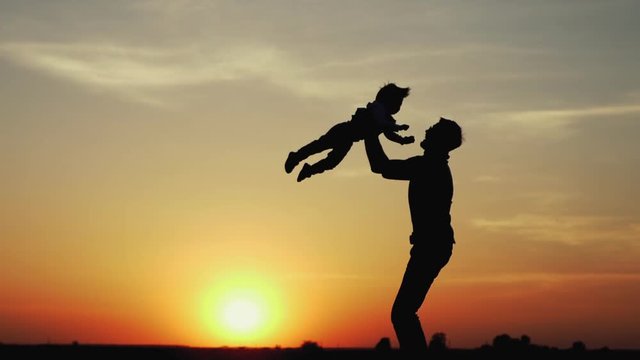 Happy child rushes into hands of father. Family hugs over sunset sky background. Silhouettes of anonymous boy and man outside in summer or autumn landscape. Slow motion 180fps