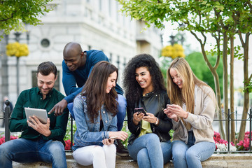 Multi-ethnic young people using smartphone and tablet computers outdoors