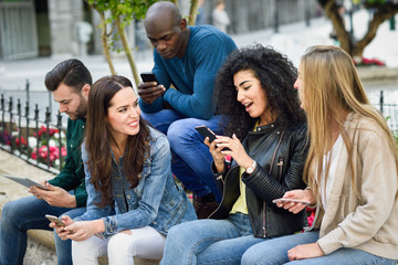 Multi-ethnic young people using smartphone and tablet computers outdoors