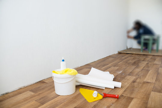 Woman glues white wallpaper in the room with a brush and roller
