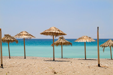 Straw parasols on a beach, in the background a turquoise sea