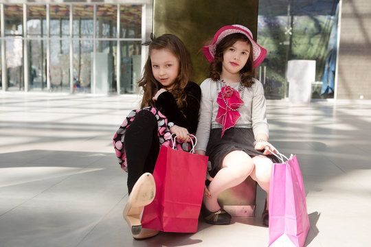 two Cheerful  little girls walking with shopping bags. two pretty girls in dresses and sunglasses near shopping mall having fun. 