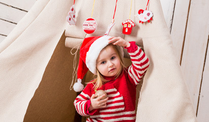 cute little girl in red santa hat over her eyes with toy-ball in hands near wigwam © Ievgen Skrypko