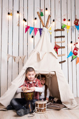 Kids playing drum sitting inside wigwam in decorated wooden room    © Ievgen Skrypko