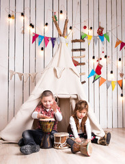 Kids playing drum sitting inside wigwam in decorated wooden room © Ievgen Skrypko