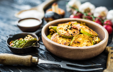 close-up of fried zucchini in stoneware with spices on wooden table