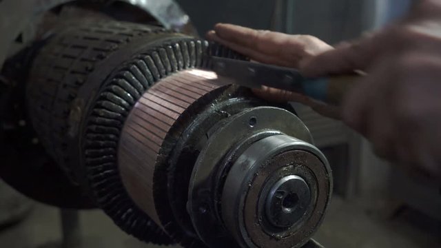Mechanic repairing rotor of electric motor .Processes with a file.