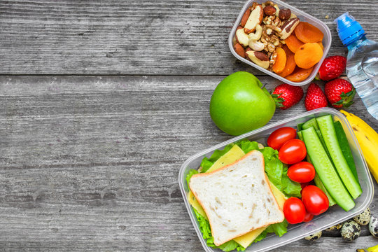 Healthy lunch boxes with sandwich, eggs and fresh vegetables, bottle of water, nuts and fruits
