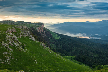 View from above on mountain forests and distant valley covered with glowing clouds and mist at sunset. Lagonaki, Caucasus, Russia