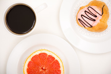 Closeup of a grapefruit versus cake with black coffee on white background
