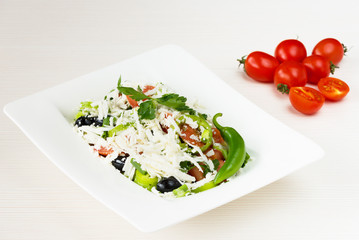 Traditional classic Shopska salad with tomatoes, peppers, cucumbers and cheese in white dish on white wooden table. Bulgarian cuisine, Balkan culture