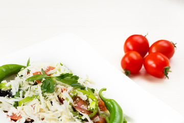 Traditional classic Shopska salad with tomatoes, peppers, cucumbers and cheese in white dish on white wooden table. Bulgarian cuisine, Balkan culture