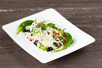 Traditional classic Shopska salad with tomatoes, peppers, cucumbers and cheese in white dish on grey wooden table. Bulgarian cuisine, Balkan culture
