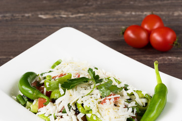 Traditional classic Shopska salad with tomatoes, peppers, cucumbers and cheese in white dish on grey wooden table. Bulgarian cuisine, Balkan culture