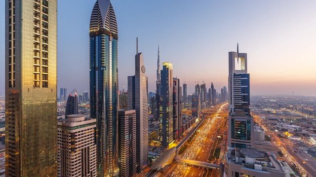 Downtown Dubai skyscrapers at sunset. Scenic aerial view of famous highway with fast moving traffic. 4K day-to-night transition time lapse.