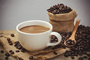 Hot Coffee cup with Coffee beans on the wooden table and the black background, vintage style color effect