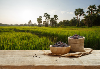 Obraz premium Rice berry in bowl and sack on wooden table with the rice field background