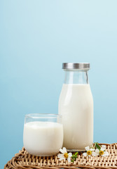 A bottle of milk and glass of milk on a wicker table on a blue background