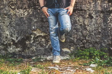 Man standing by the old stone wall, wearing blue ripped jeans and canvas sneakers