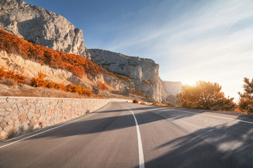 Asphalt road in autumn at sunrise. Landscape with beautiful empty mountain road with a perfect asphalt, high rocks, trees and sunny sky. Vintage toning. Travel background. Highway at mountains. Speed