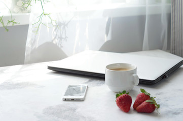 Workspace. Laptop coffee your strawberries on a white table. The view from the top. Free space