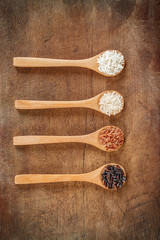 colorful brown rice in wooden teaspoons on wood background