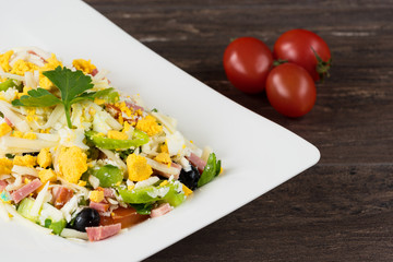 Traditional Bulgarian Shepherd salad with tomatoes, peppers, cucumbers, mushrooms, ham, cheese and eggs in white dish on grey wooden table. Bulgarian cuisine, Balkan culture