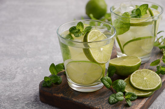 Cold refreshing summer drink with lime and mint in a glass on a grey concrete or stone background.