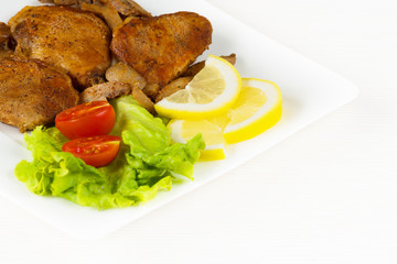 Pork fillet steak with cherry tomatoes, lemon and a lettuce in white dish on white background
