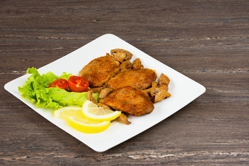 Pork fillet steak with cherry tomatoes, lemon and a lettuce in white dish on grey background.