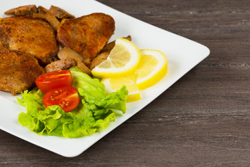 Pork fillet steak with cherry tomatoes, lemon and a lettuce in white dish on grey background.
