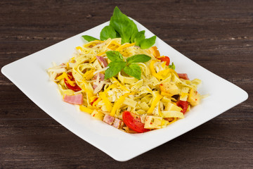 Tagliatelle pasta with pesto sauce, bacon, Gauda, Cheddar, Emmental cheese and basil leaves in white plate on grey wooden background. Close up image - healthy homemade pasta.