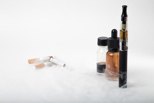 Broken tobacco cigarettes with modern electronic cigarette and e-juice bottles with smoke