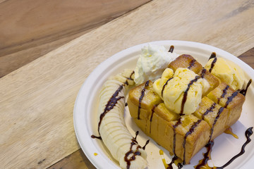 honey toast ice cream with whipped cream and banana on bread topped with honey and chocolate in white paper dish on the wood table for dessert sweet and warm white with copyspace