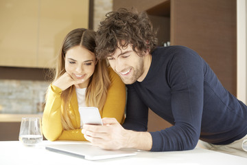 Getting some good news on mobile phone. Shot of a lovely young couple using smartphone while relaxing at home. 