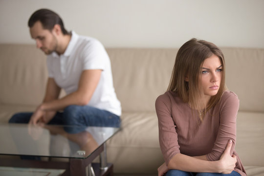 Sad couple not talking to each other after quarrel. Pensive upset woman feeling offended, thinking over problems in relationships, anxious about future, upset man sitting in the background