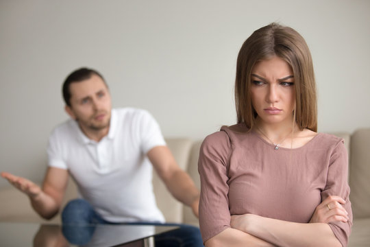 Unhappy family couple quarreling, angry husband complaining and blaming wife for problems, frustrated woman disagrees standing silent with arms crossed. Marital misunderstandings, lack of dialogue