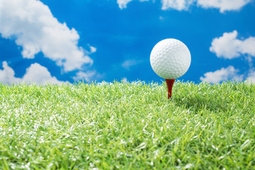 golf ball on red tee on green fake grass against sunny cloud and blue sky background