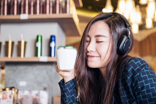 A beautiful Asian woman close her eyes and listening to music with headphone while drinking coffee with feeling happy and relax in modern cafe