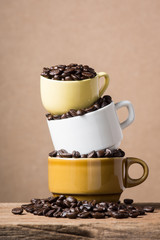 coffee beans spilled from pile of three coffee cup against brown background