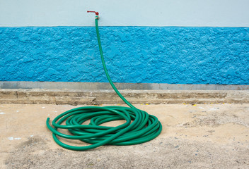roll of green multipurpose hose connected on faucet at wall