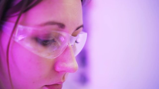 Close up of a woman scientist in protective glasses looking at vials and in her notes. Handheld real time close up shot