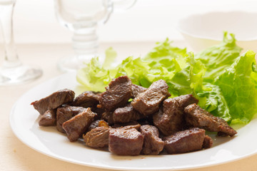 Fried beef goulash with a leaf of lettuce on a white plate. Tasty and nutritious dish.