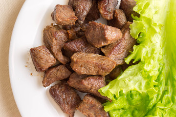 Fried beef goulash with a leaf of lettuce on a white plate. Tasty and nutritious dish.