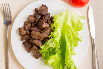 Fried beef goulash with a leaf of lettuce on a white plate. Tasty and nutritious dish.