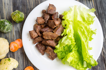 Fried beef goulash with lettuce leaves on a white plate and frozen vegetables. Tasty and nutritious...