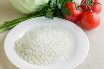 Raw rice in a plate and vegetables. Ingredients for cooking.